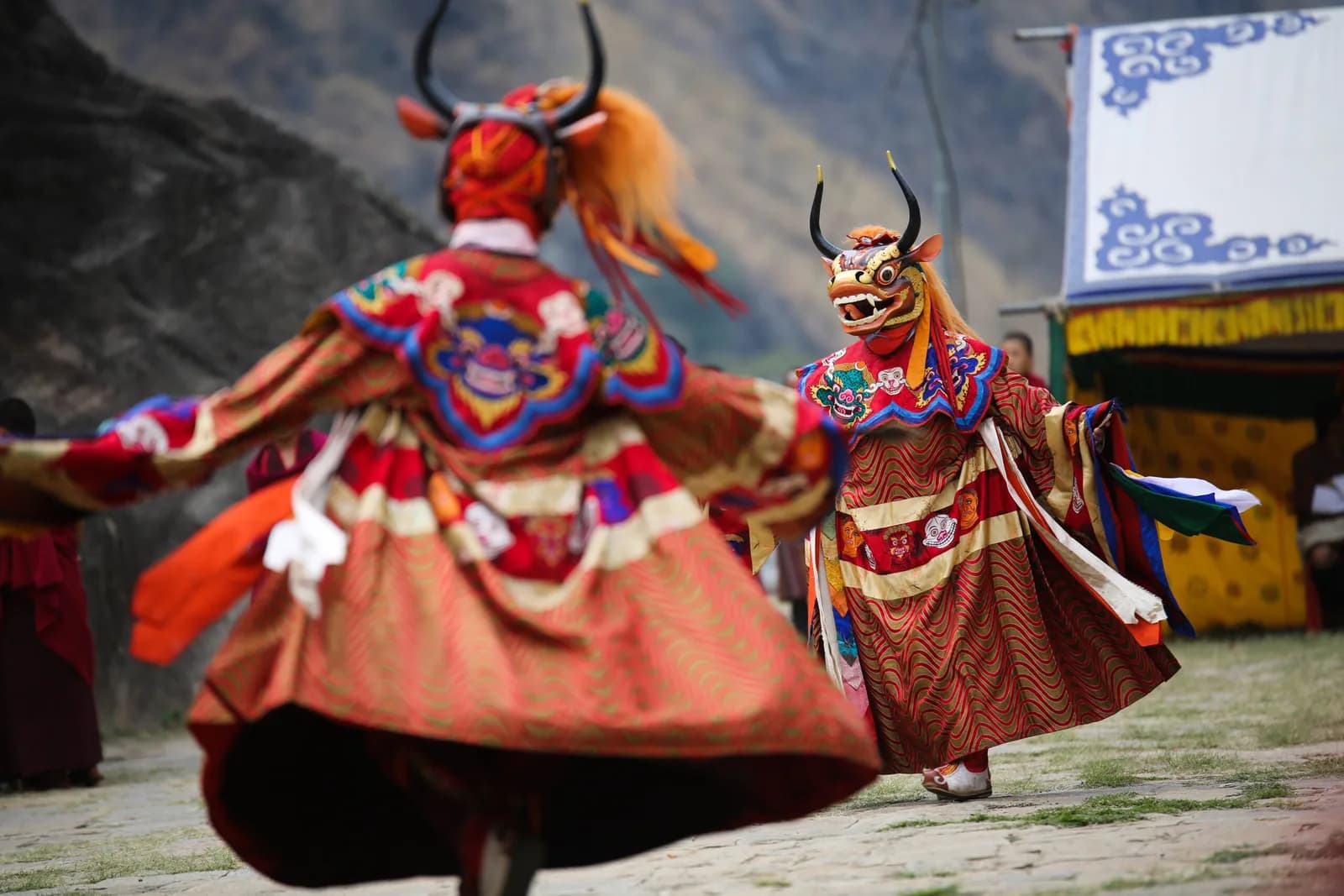 Cham dancers in horned masks and brocade aprons turning through the Paro Tshechu courtyard