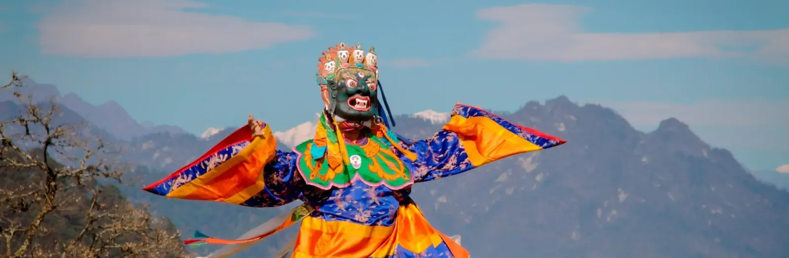 Masked cham dancers in red and yellow costumes turning inside a dzong courtyard during a tshechu