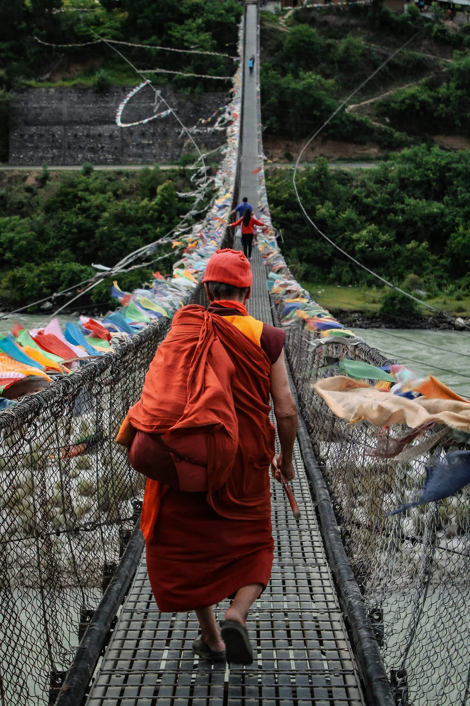 Crossing the long prayer-flag iron suspension bridge over the Pho Chhu river in warm Punakha valley